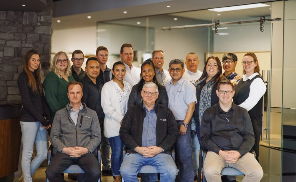 Group photo of the Virta Gloves team, featuring a diverse group of men and women standing and seated together in a modern office setting, smiling at the camera.