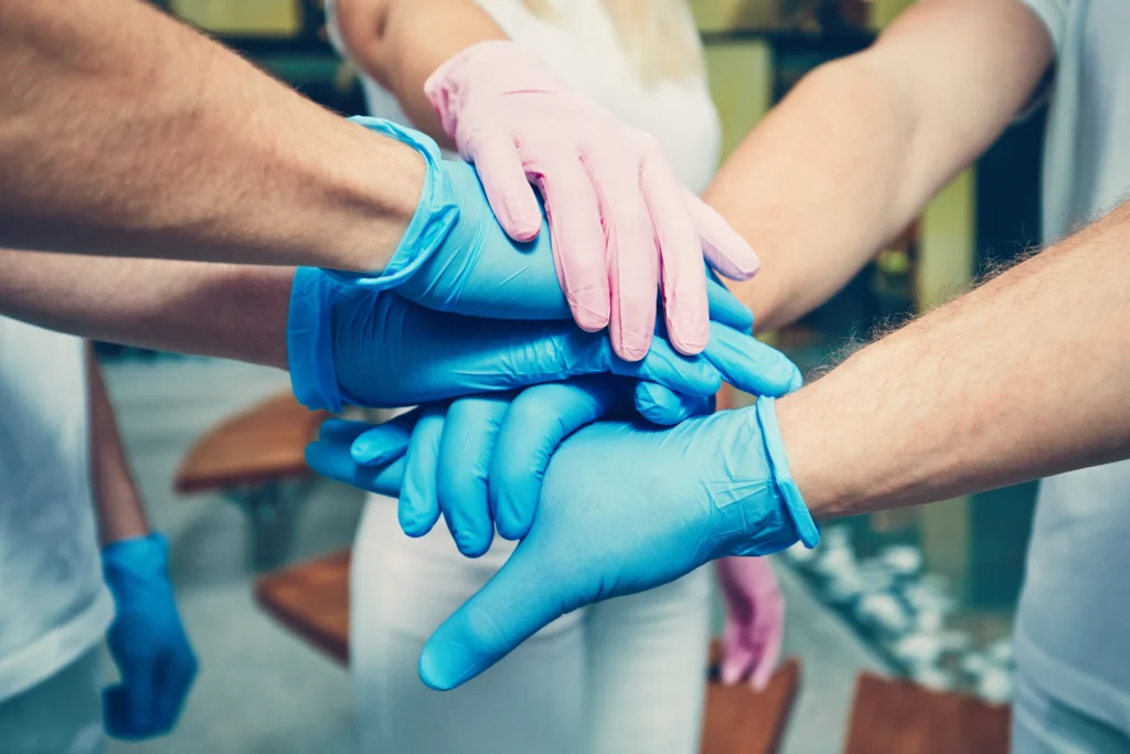 group of healthcare professionals grouped together and joined their hands together while wearing a nitrile gloves